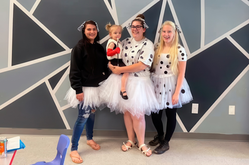 three women in playful polka dot outfits pose with a girl in a cute costume, celebrating together in a fun atmosphere.