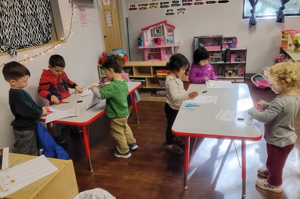 A group of young children engages in a crafting activity at tables, focused on their projects with a variety of supplies.