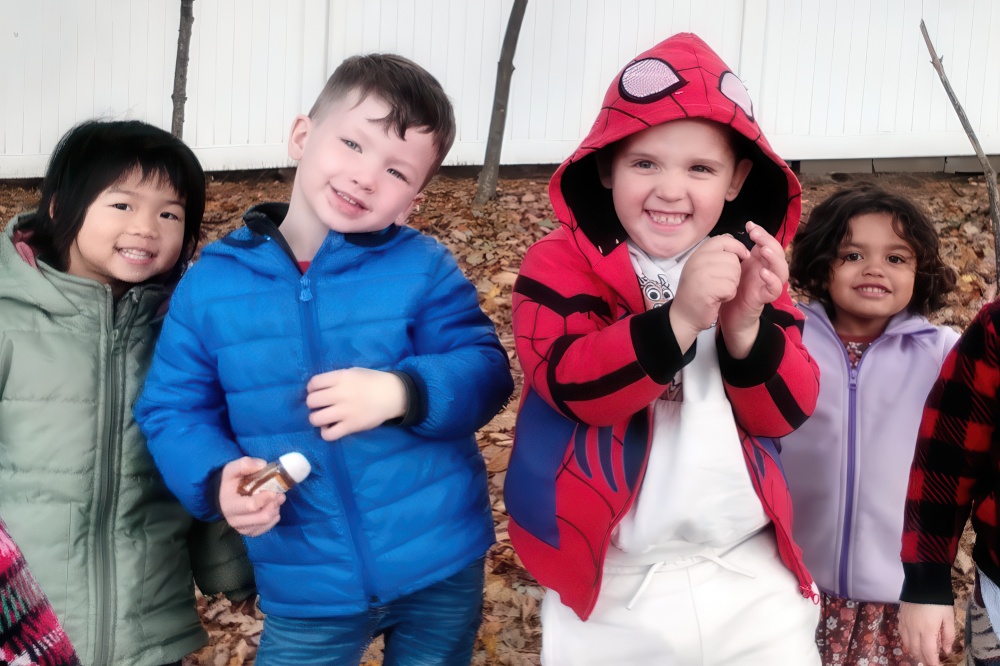 A group of smiling children poses outdoors amidst autumn leaves, showcasing their vibrant jackets and cheerful expressions.