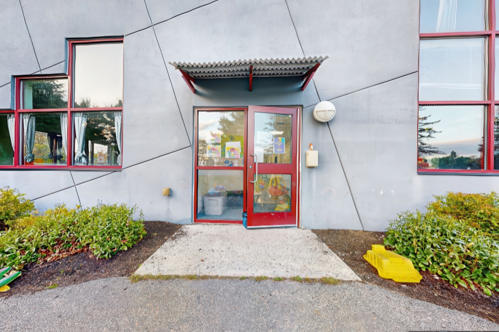 The entrance to a building with large windows and a welcoming door, surrounded by neat landscaping.