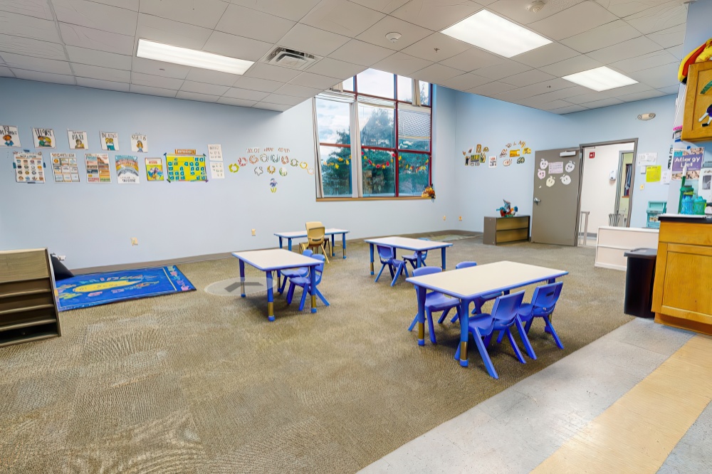 A spacious classroom with light blue walls, empty tables, and educational decorations, creating a welcoming atmosphere.