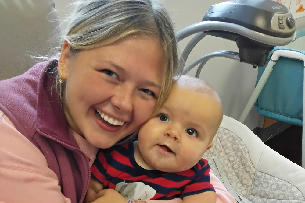 A young parent shares a warm smile with her baby, both looking happy and cozy in a nurturing environment.