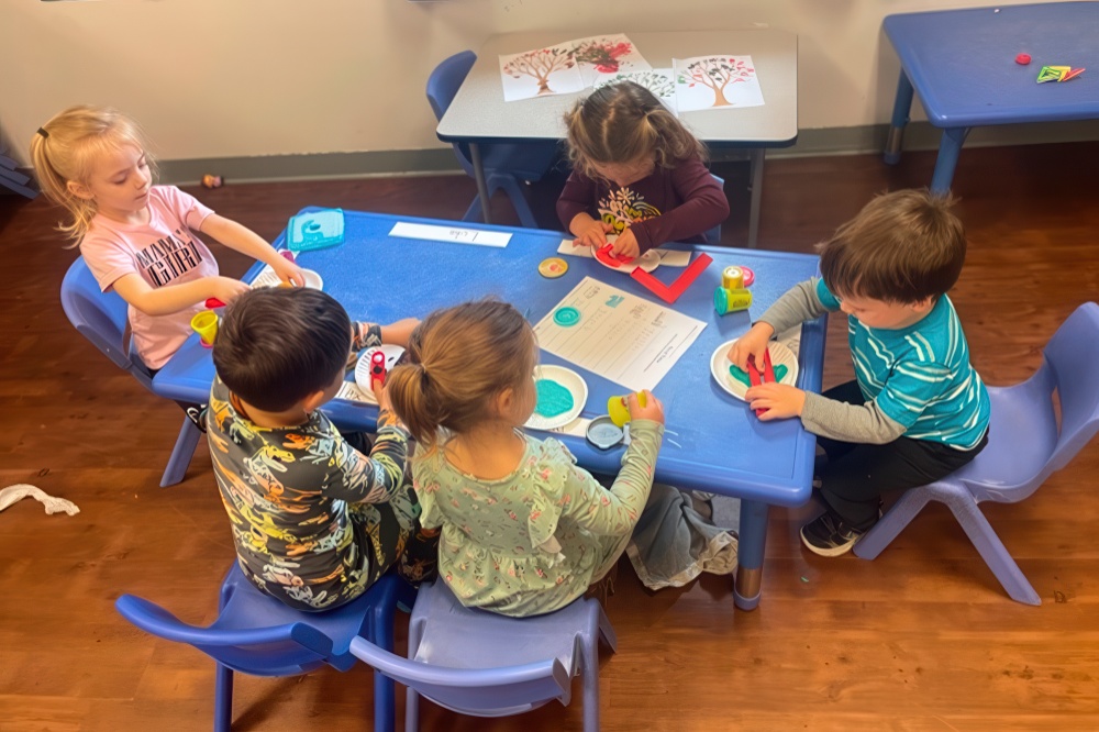 A group of young children gather around a table, happily engaging in creative play with colorful materials and crafts.