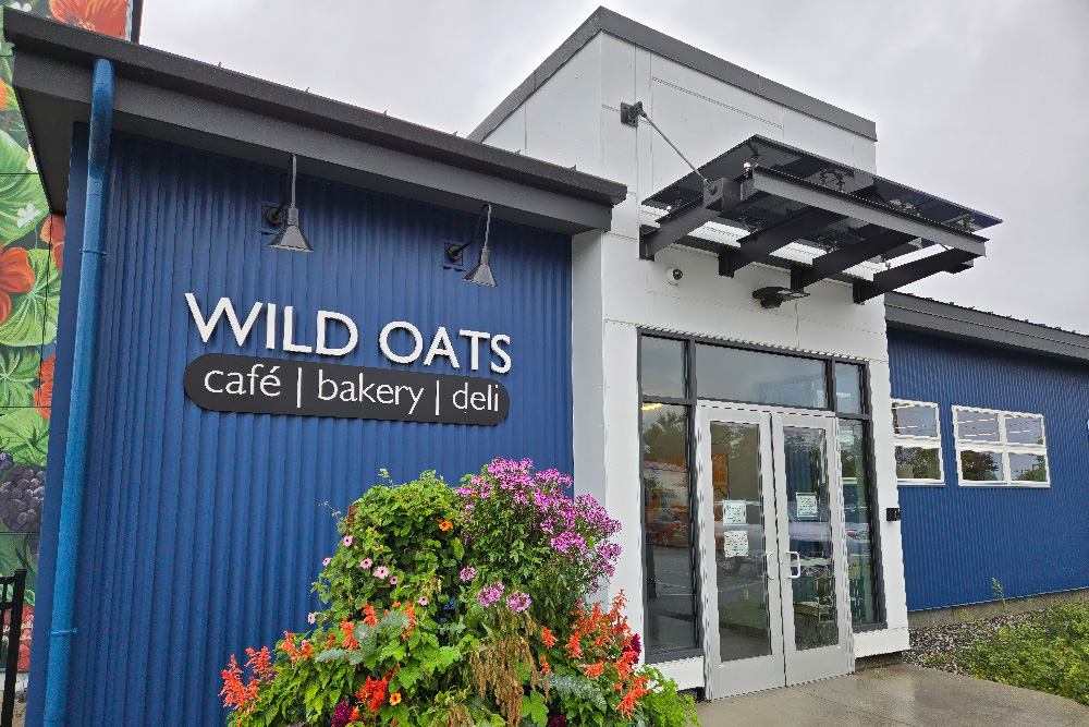 The entrance of Wild Oats café, bakery, and deli, featuring a modern design with vibrant flowers at the base.