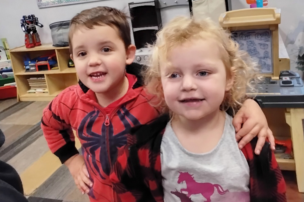 A boy and a girl smile for the camera, the boy in a Spider-Man shirt and the girl in a unicorn top, sharing a joyful moment.