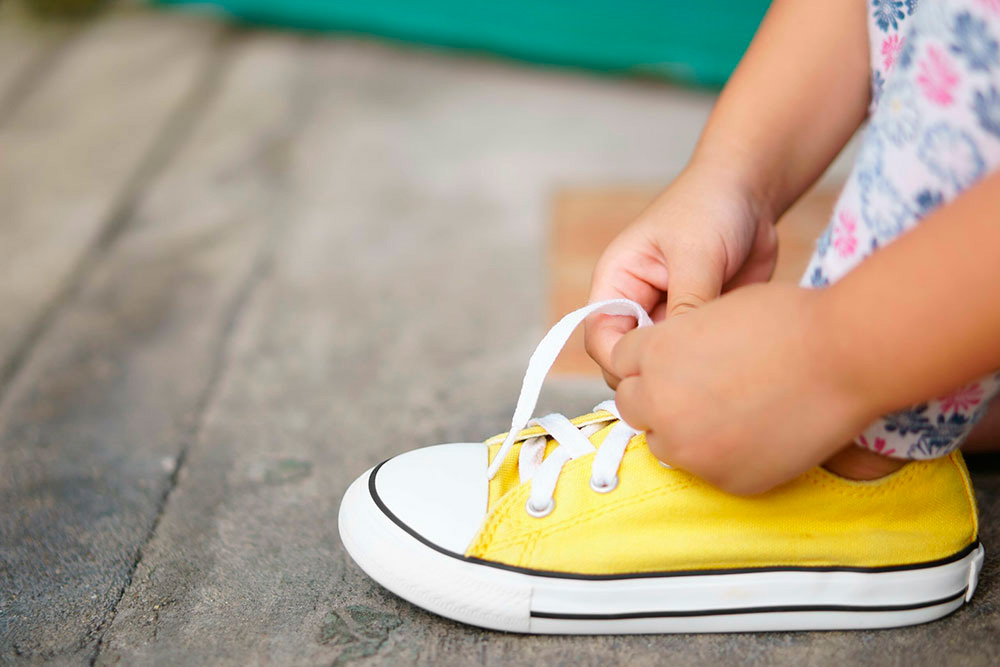 A child's hand is tying the laces of a bright yellow sneaker, showcasing a moment of independence.