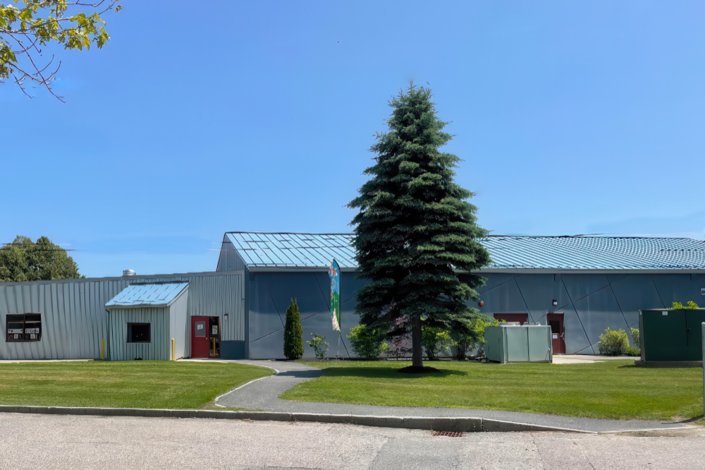 An exterior view of a building with a green lawn and a tall tree, showcasing a clear blue sky overhead.