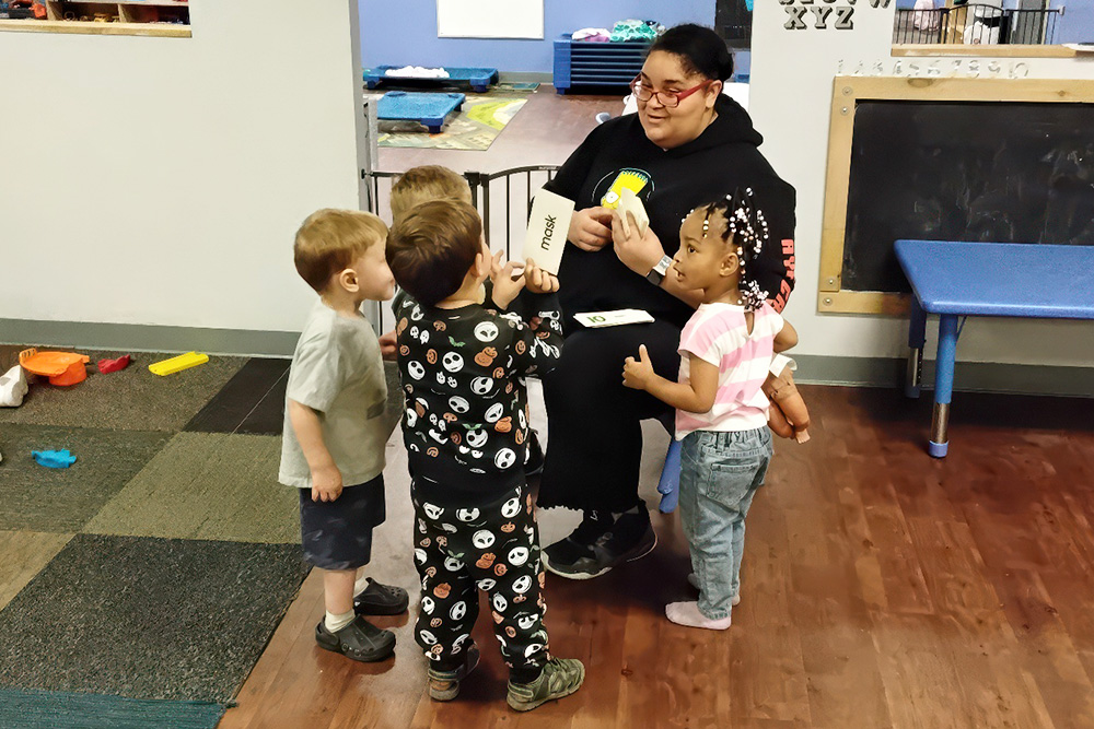 A teacher engages with four children, using flashcards in a classroom setting, fostering learning and interaction.