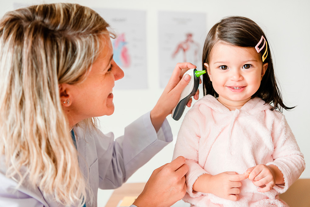 A teacher gently checking child's ear for temperature, both smiling, in a warm, nurturing environment.