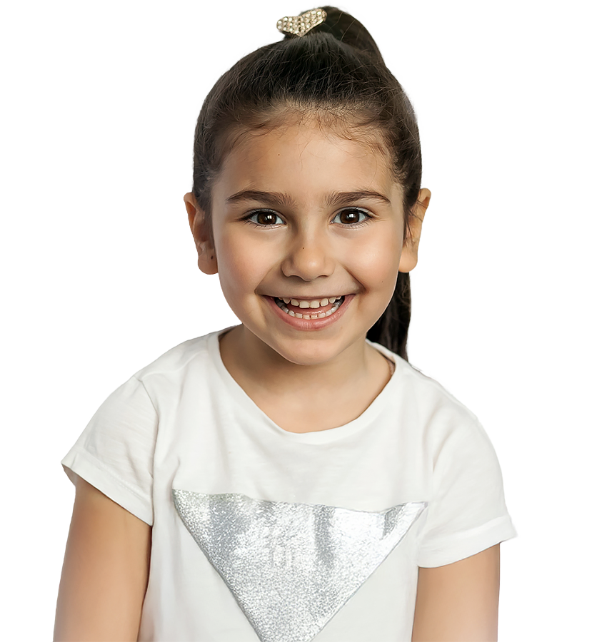 A young girl with a bright smile poses for the camera, wearing a white shirt with a shiny design.