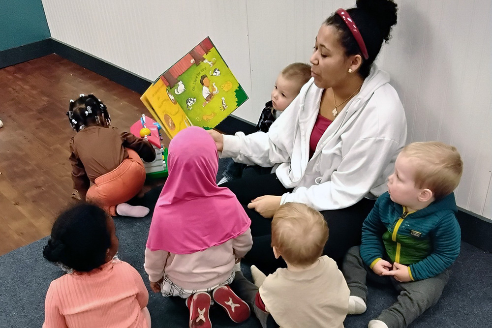 A teacher engages toddlers during storytime, with children sitting around her, focused on the colorful book.