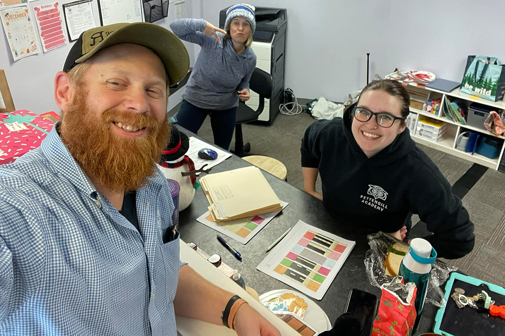 Three adults take a cheerful selfie in an office setting, surrounded by supplies, showcasing a fun.