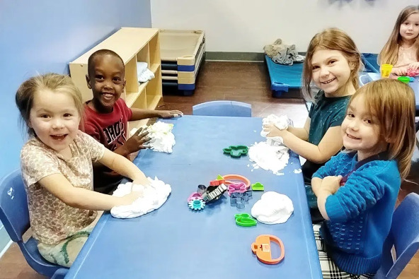 Four children are engaged in a playful activity at a table, using fluffy materials and various colorful toys.