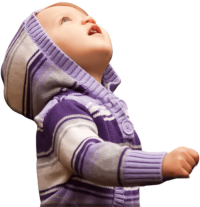 Young child in purple striped sweater looking up at sky while sitting among autumn leaves in a forest.